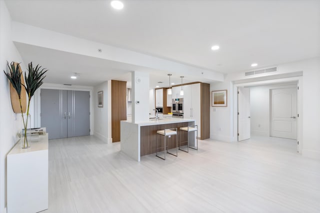 kitchen with a breakfast bar, a sink, light countertops, hanging light fixtures, and a center island with sink