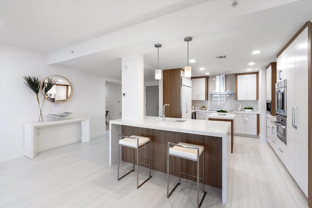 kitchen with a sink, white cabinetry, light countertops, hanging light fixtures, and wall chimney exhaust hood