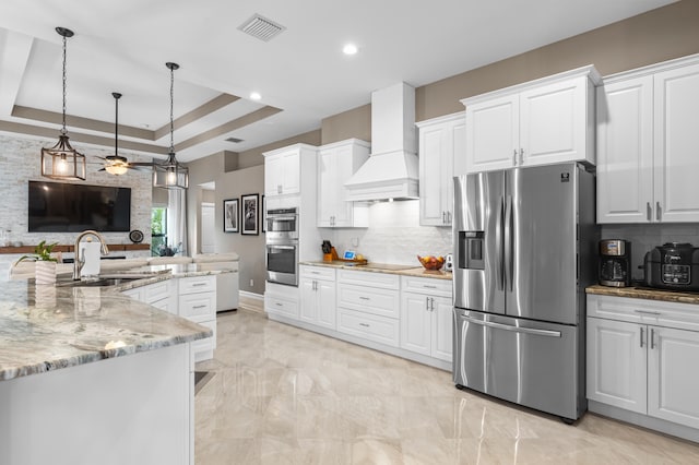 kitchen featuring appliances with stainless steel finishes, a raised ceiling, white cabinets, and custom exhaust hood