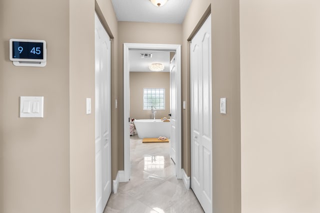 corridor with visible vents, a textured ceiling, and baseboards