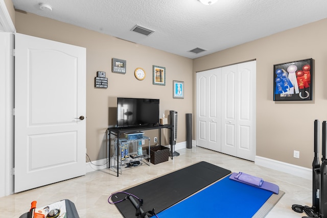 exercise area featuring visible vents, a textured ceiling, and baseboards