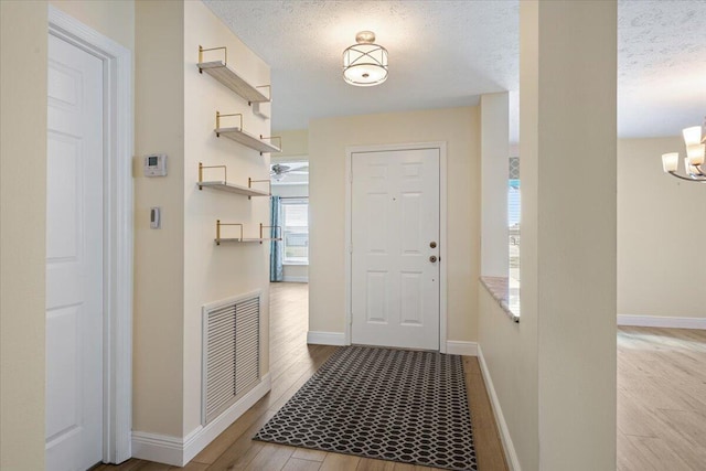 doorway featuring baseboards, visible vents, an inviting chandelier, a textured ceiling, and light wood-style floors