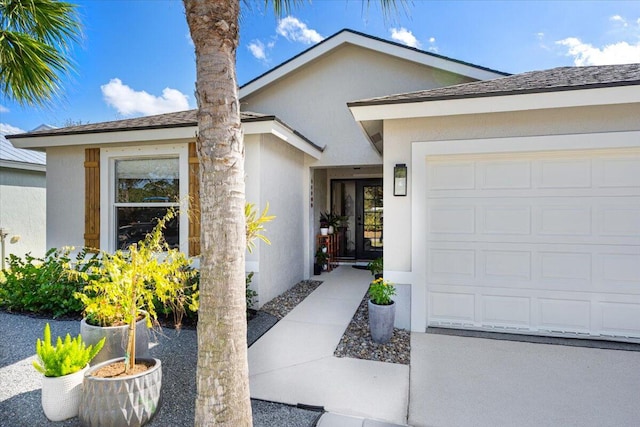 property entrance featuring a shingled roof, an attached garage, and stucco siding