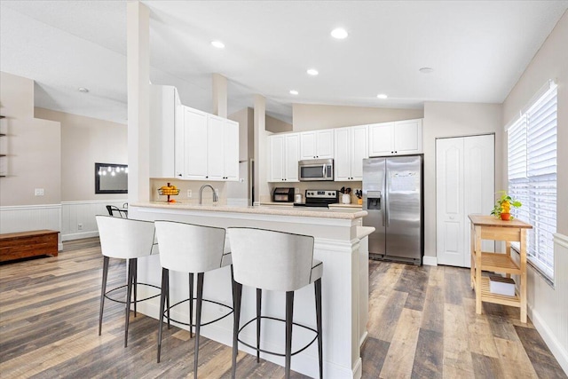 kitchen with stainless steel appliances, a peninsula, white cabinets, vaulted ceiling, and a kitchen breakfast bar