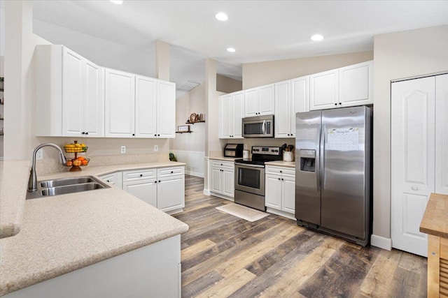 kitchen with wood finished floors, vaulted ceiling, stainless steel appliances, white cabinetry, and a sink