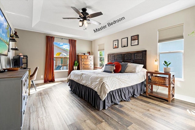 bedroom featuring a raised ceiling, baseboards, ceiling fan, and light wood finished floors