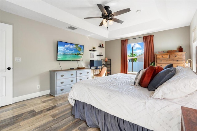 bedroom with a raised ceiling, visible vents, ceiling fan, wood finished floors, and baseboards