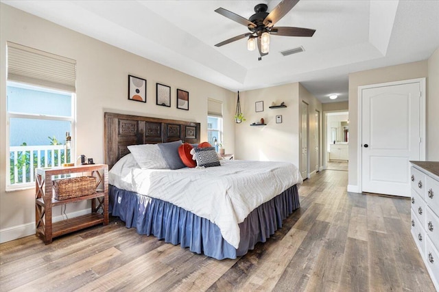 bedroom with multiple windows, visible vents, a tray ceiling, and wood finished floors