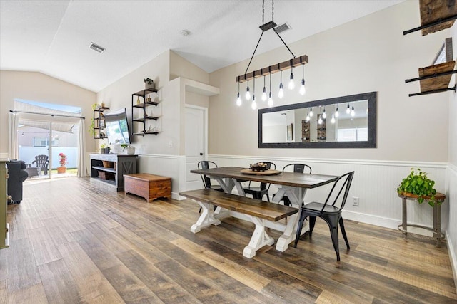 dining room with lofted ceiling, visible vents, wood finished floors, and wainscoting