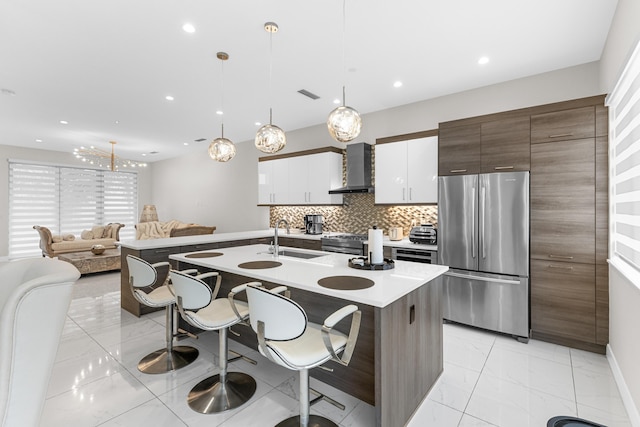 kitchen featuring decorative light fixtures, stainless steel appliances, white cabinetry, a sink, and wall chimney range hood