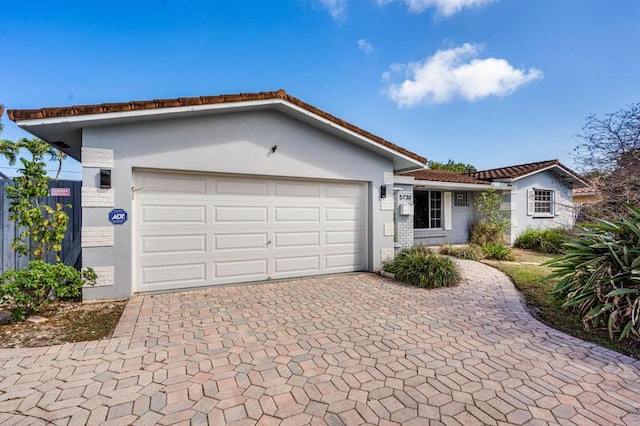 single story home with a garage, brick siding, decorative driveway, and stucco siding