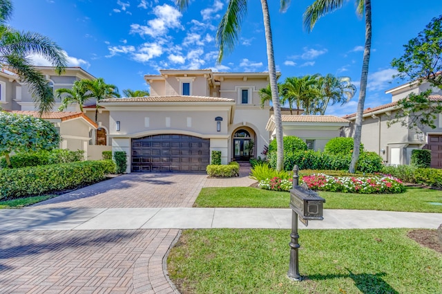 mediterranean / spanish-style home with a garage, a tiled roof, decorative driveway, stucco siding, and a front yard