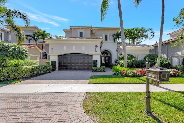 mediterranean / spanish home featuring a garage, a tile roof, decorative driveway, stucco siding, and a front lawn