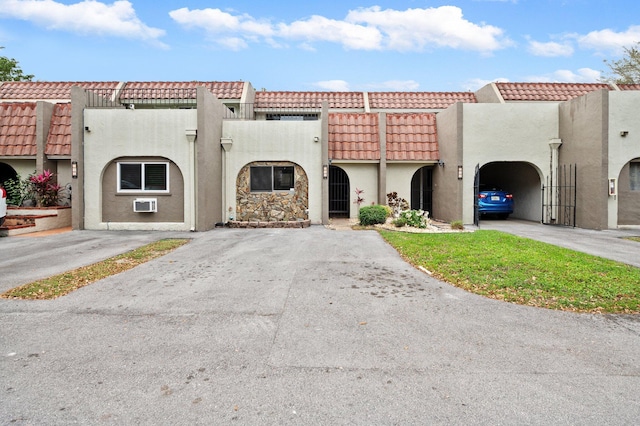 view of front of property featuring driveway, a tile roof, a wall unit AC, and stucco siding