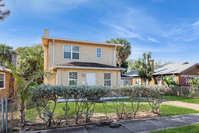 traditional-style house featuring a front yard, fence, and stucco siding