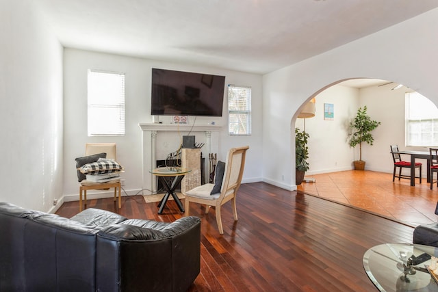 living area featuring arched walkways, a fireplace with flush hearth, wood finished floors, and a healthy amount of sunlight