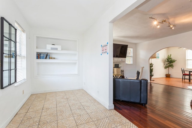 interior space with arched walkways, built in shelves, light wood finished floors, and baseboards