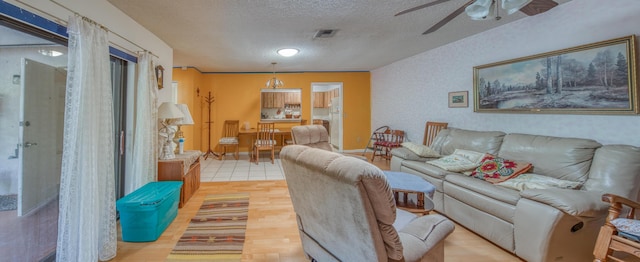 living area with light wood finished floors, visible vents, baseboards, ceiling fan, and a textured ceiling