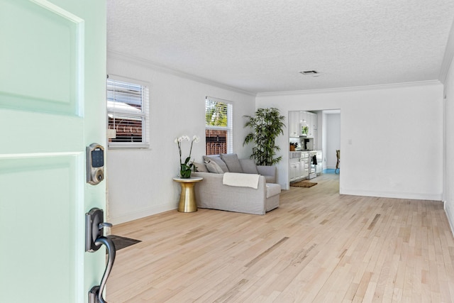 sitting room with visible vents, ornamental molding, a textured ceiling, light wood-type flooring, and baseboards