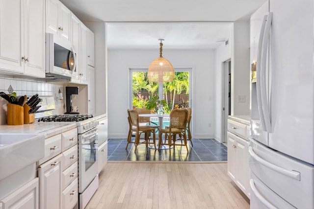 kitchen featuring light wood-style flooring, white appliances, white cabinetry, backsplash, and decorative light fixtures