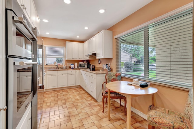 kitchen with a healthy amount of sunlight, white cabinets, stainless steel double oven, and recessed lighting