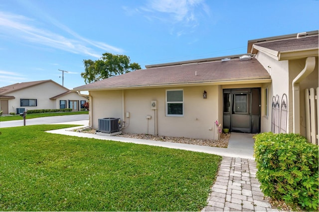 back of property with stucco siding, a lawn, and central air condition unit