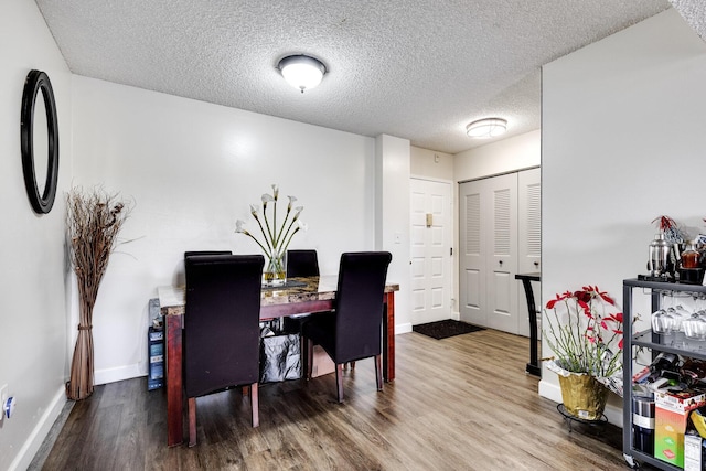 dining area with a textured ceiling, baseboards, and wood finished floors