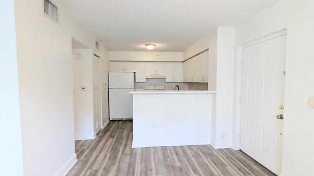 kitchen with visible vents, freestanding refrigerator, light countertops, a textured ceiling, and under cabinet range hood