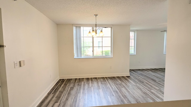 unfurnished dining area with a textured ceiling, wood finished floors, and baseboards