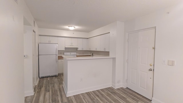 kitchen featuring a peninsula, light wood-style floors, white cabinets, light countertops, and freestanding refrigerator