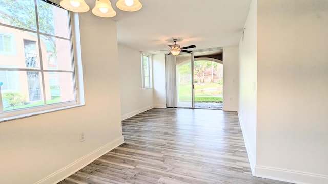 unfurnished room with ceiling fan with notable chandelier, light wood-style flooring, and baseboards