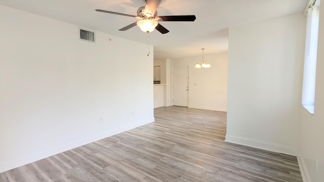 unfurnished room featuring ceiling fan with notable chandelier, visible vents, baseboards, and wood finished floors