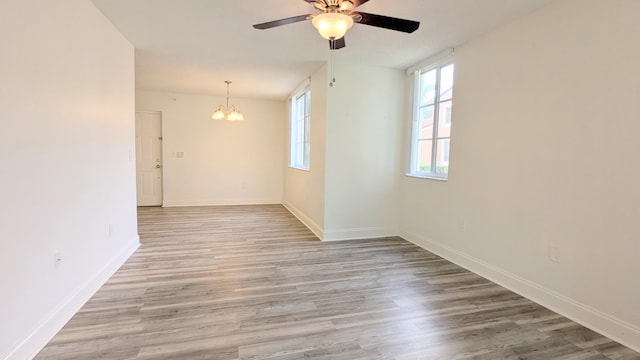 empty room featuring ceiling fan with notable chandelier, light wood-type flooring, and baseboards