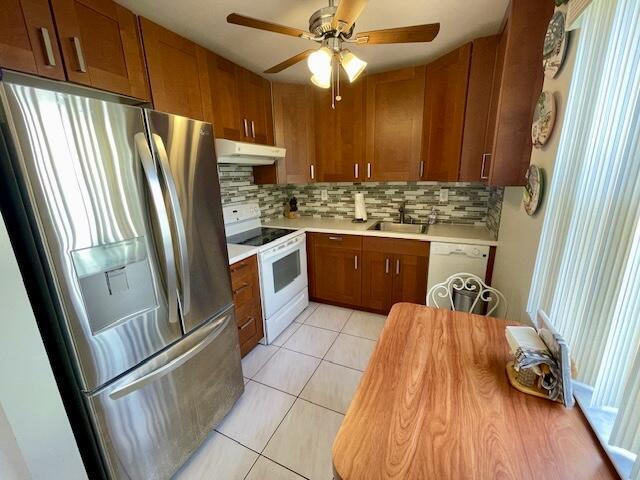 kitchen with light countertops, a sink, under cabinet range hood, and white appliances