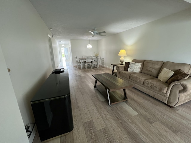 living room with baseboards, ceiling fan, a textured ceiling, and light wood finished floors