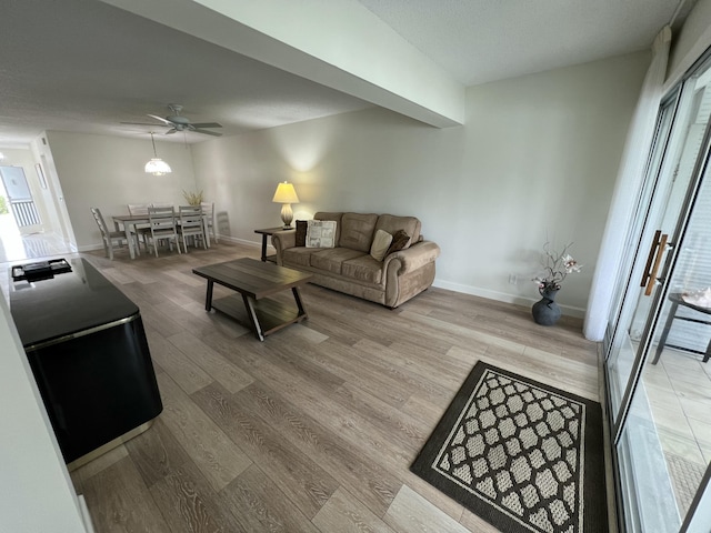 living area with light wood-type flooring, a ceiling fan, and baseboards