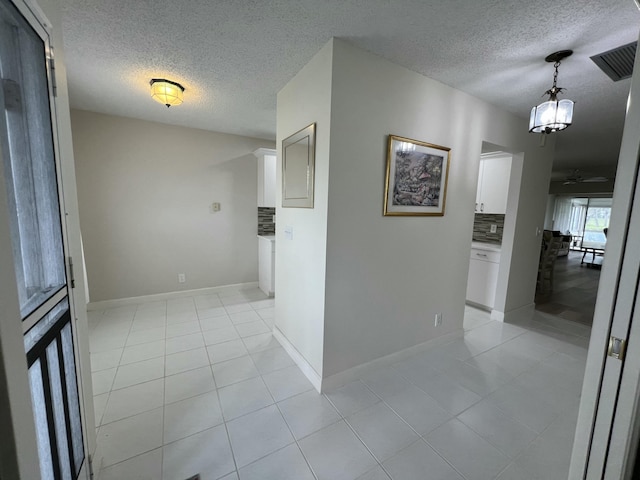 interior space featuring light tile patterned floors, baseboards, visible vents, and a textured ceiling