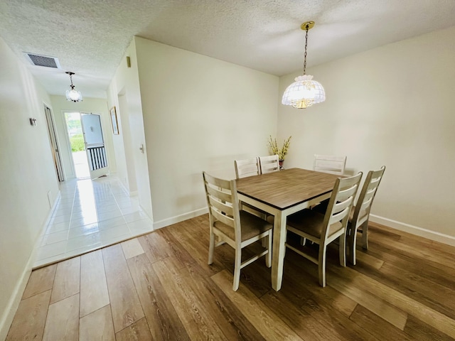 dining area with a textured ceiling, light wood-type flooring, visible vents, and baseboards