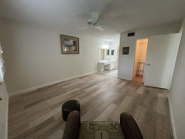 unfurnished bedroom with a textured ceiling, connected bathroom, light wood-style flooring, visible vents, and baseboards