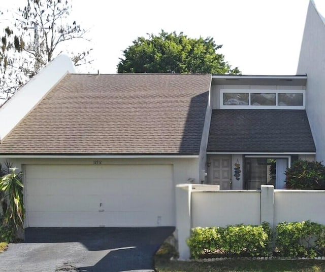 view of front of home with a garage, aphalt driveway, a fenced front yard, and a shingled roof