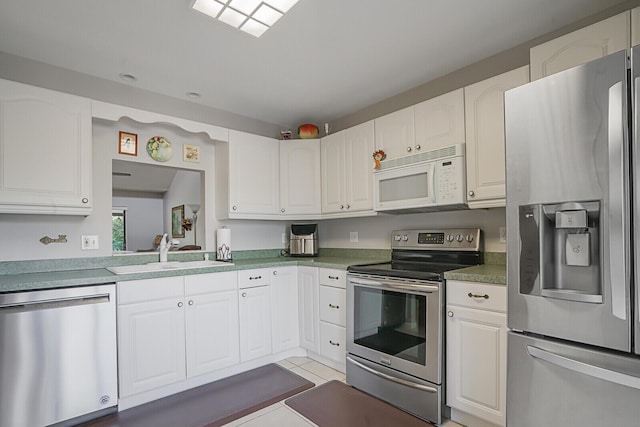 kitchen with light tile patterned floors, stainless steel appliances, light countertops, white cabinetry, and a sink