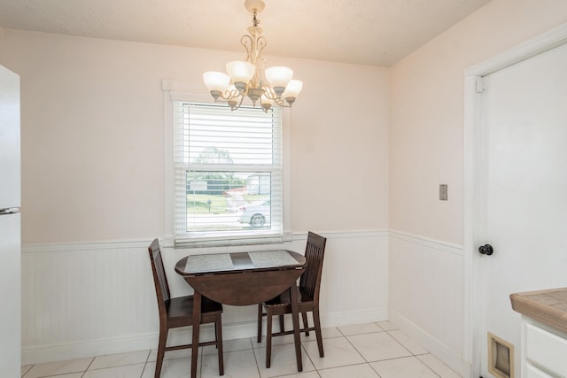 dining area with an inviting chandelier, light tile patterned floors, and wainscoting