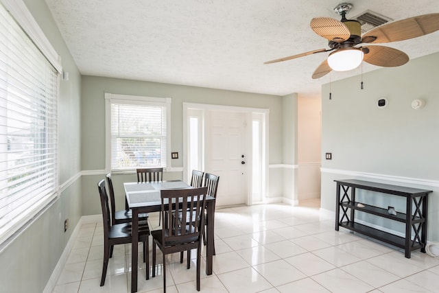 dining area featuring light tile patterned floors, a ceiling fan, baseboards, and a textured ceiling