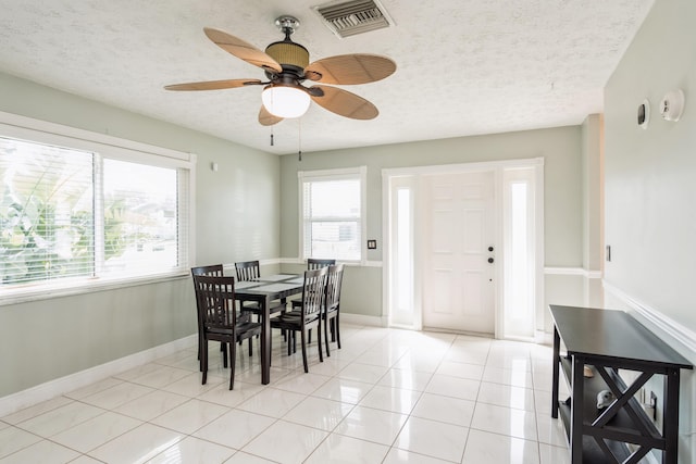 dining space with a textured ceiling, light tile patterned flooring, visible vents, and baseboards