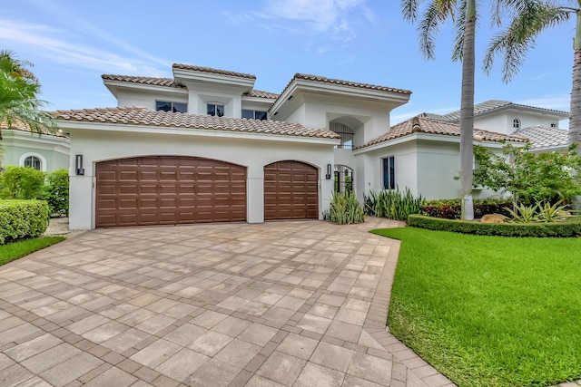 mediterranean / spanish-style home with a garage, decorative driveway, a front yard, and stucco siding