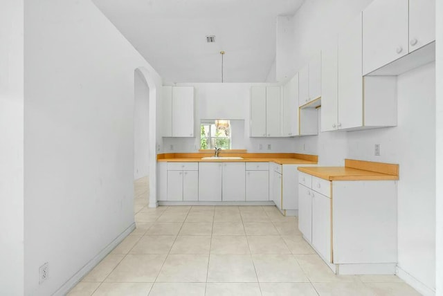 kitchen featuring arched walkways, white cabinetry, light tile patterned flooring, a sink, and light countertops