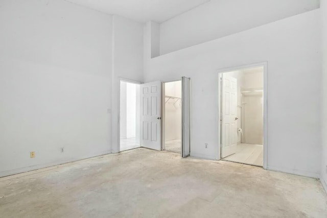 unfurnished bedroom featuring concrete floors, a closet, a high ceiling, a spacious closet, and connected bathroom