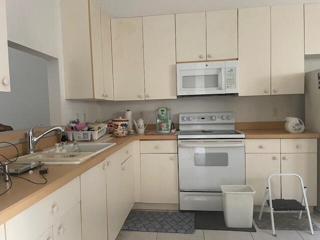 kitchen featuring white appliances, light tile patterned floors, light countertops, and a sink