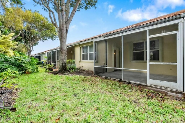 view of home's exterior with a yard, stucco siding, a sunroom, and a tile roof