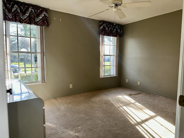 unfurnished dining area featuring light carpet, ceiling fan, baseboards, and a textured ceiling